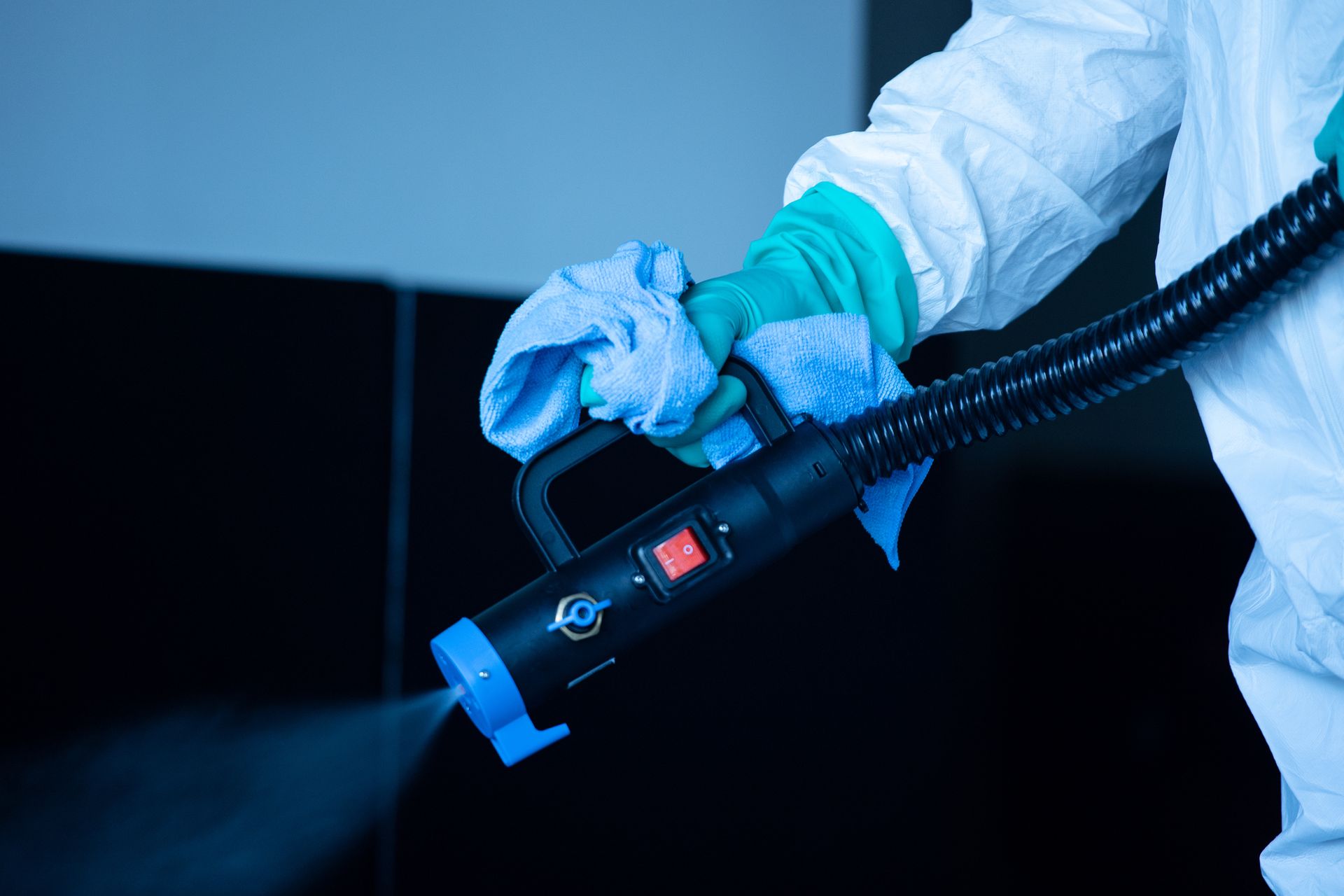 A person in a protective suit is disinfecting a room with a sprayer.