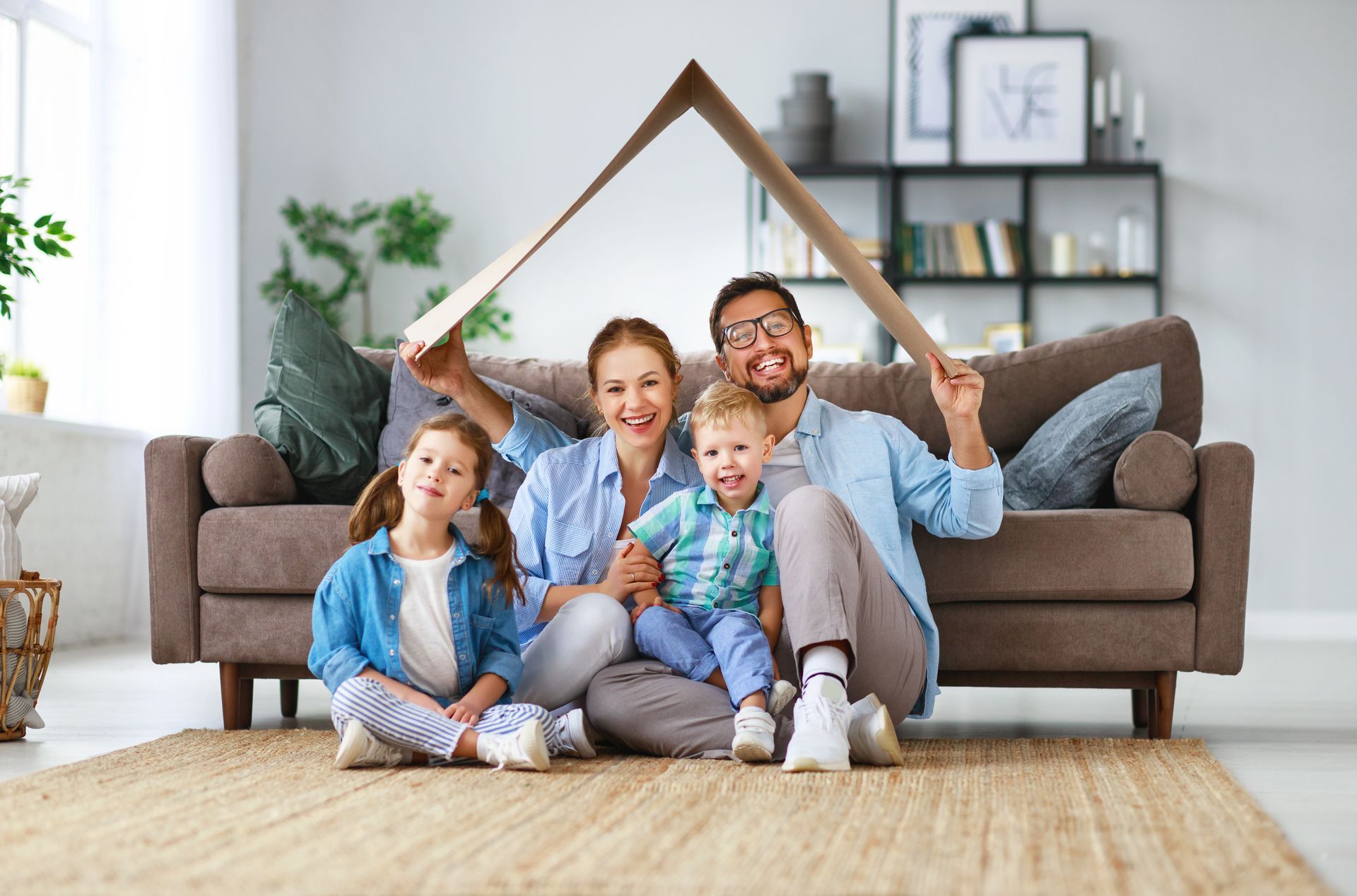 Family sitting on a couch in a bright living room, smiling and holding a roof-shaped frame above them