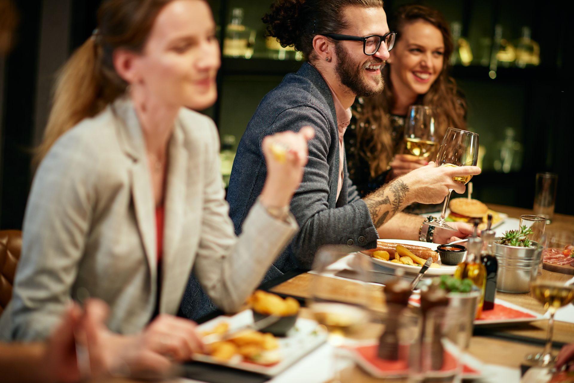 Friends dining and talking at a restaurant table with wine and plated food