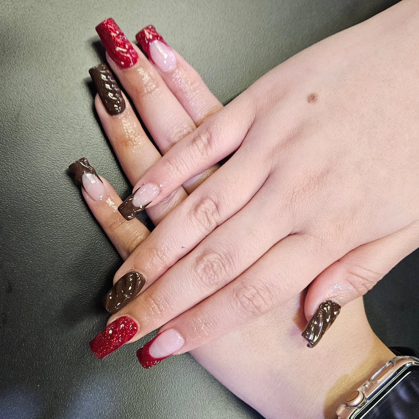 Two hands featuring long, square-shaped acrylic nails in alternating red and dark brown textured cable-knit designs.