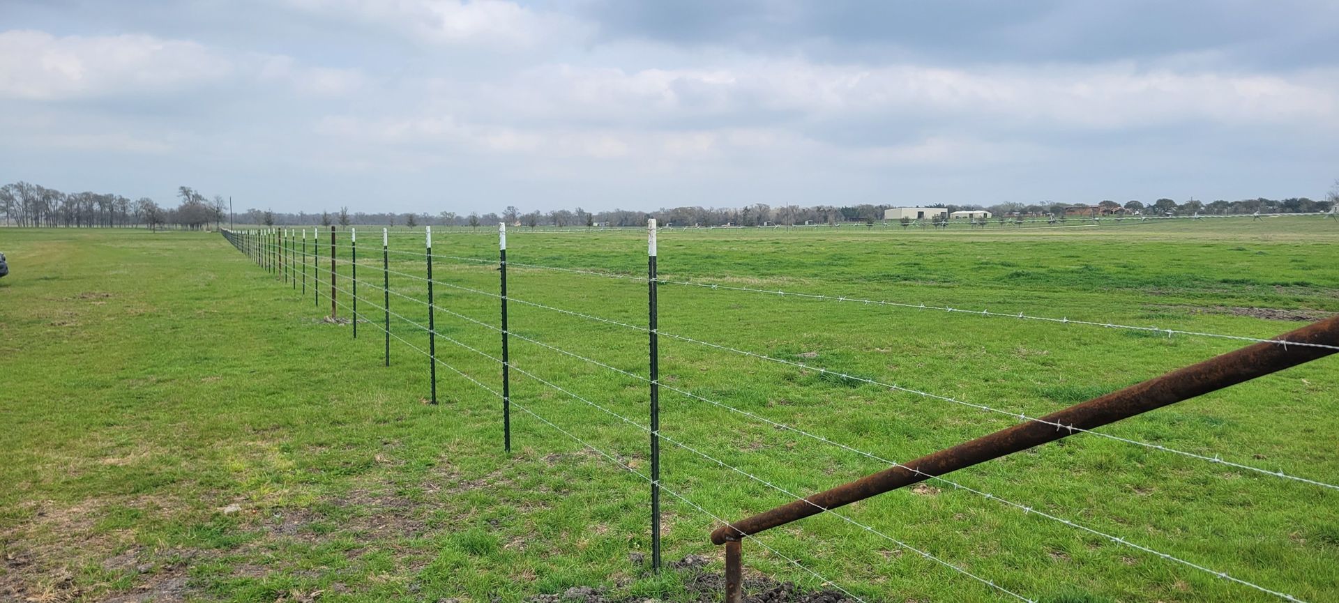 A green field with a fence in the foreground under a cloudy sky.