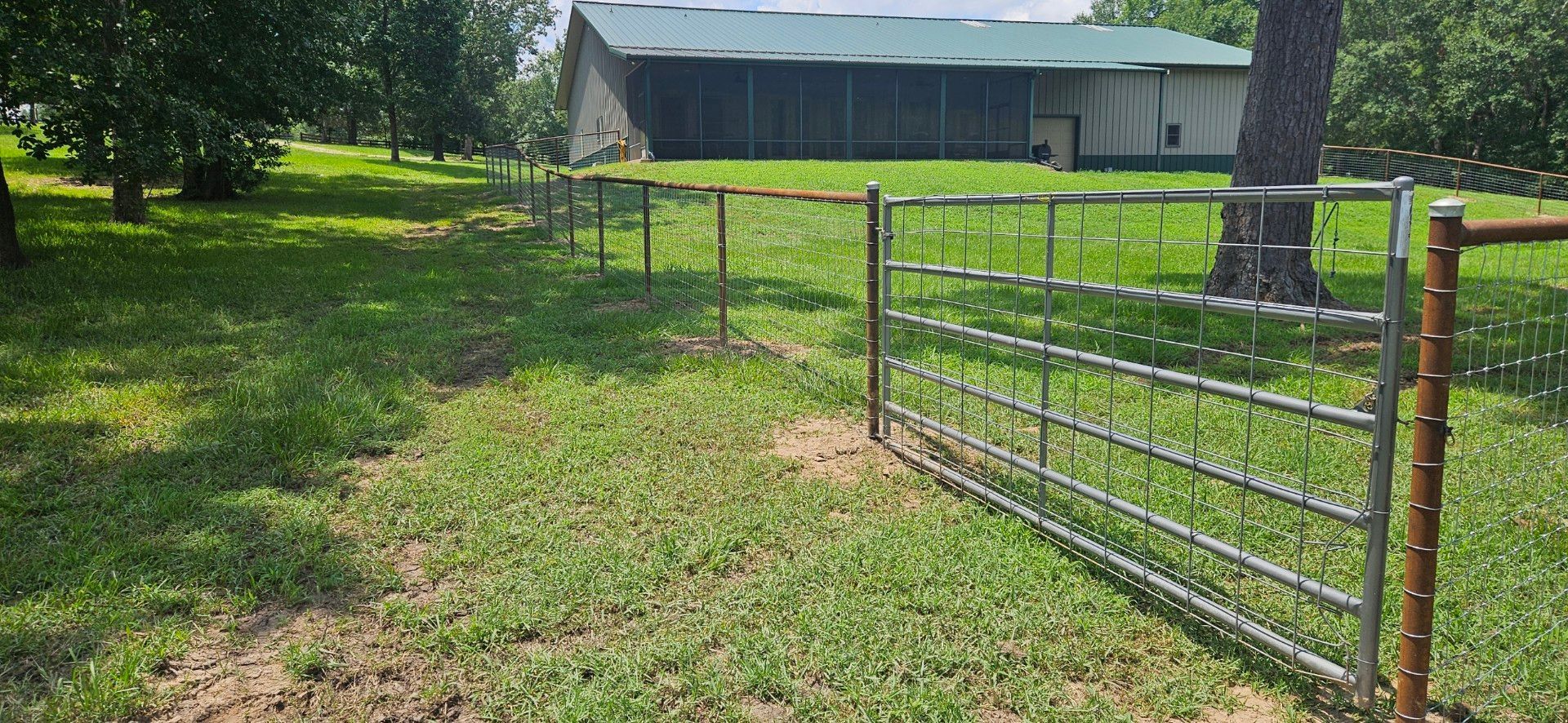 Metal gate in a grassy field, leading to a barn with a green roof.