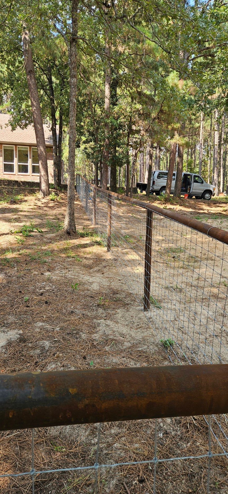 A view of a fence leading to a house. Two trucks are parked in the distance.