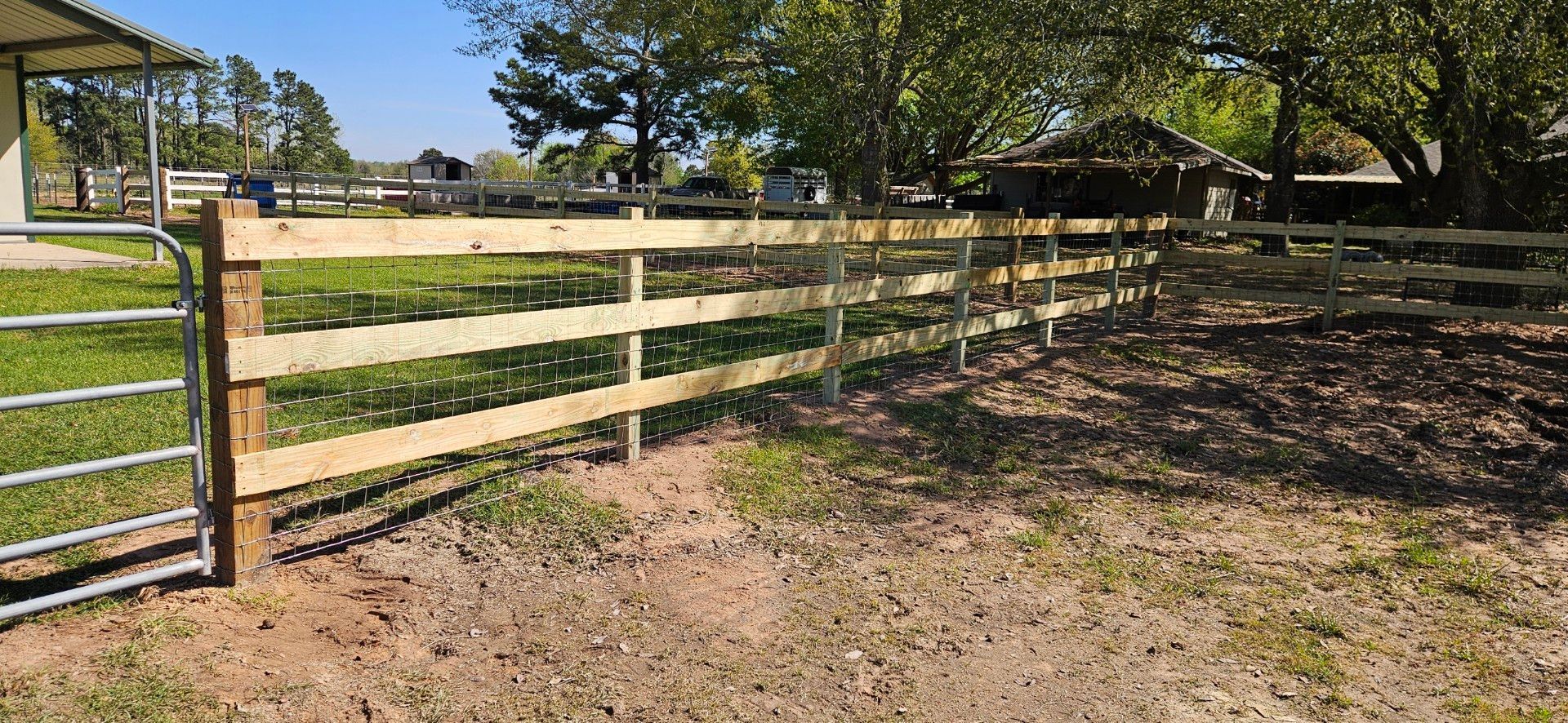 Wooden fence with gate, grassy field, trees in the background, sunny day.
