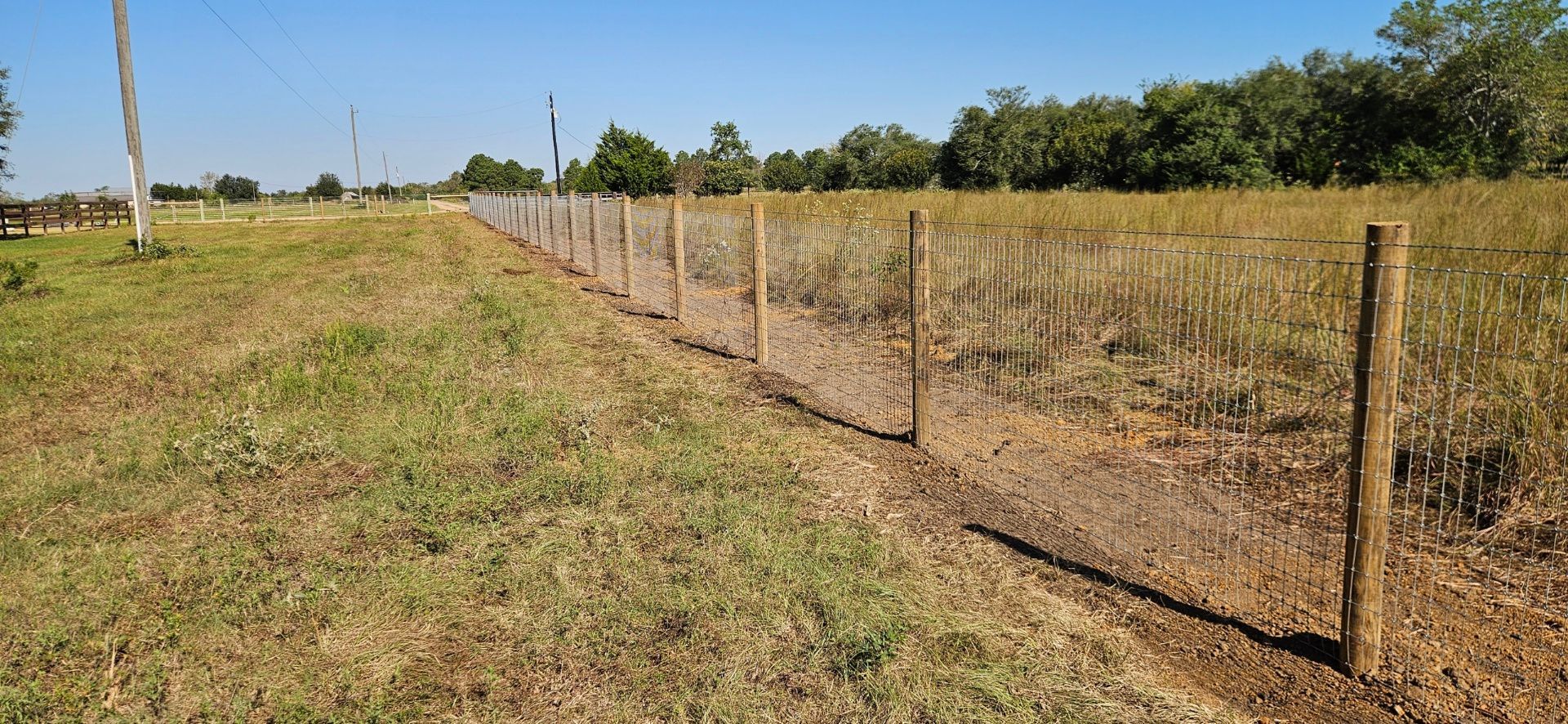 A wooden fence runs through a grassy field under a clear blue sky.