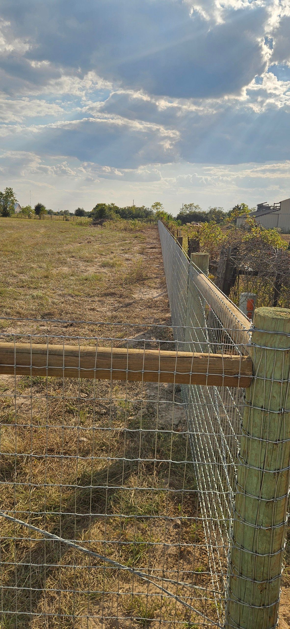 A wire fence in a field under a cloudy sky.