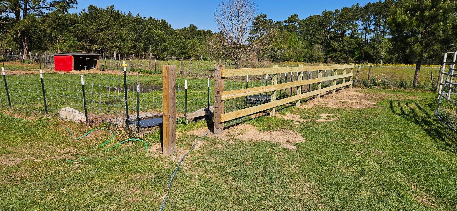 Wooden fence in a grassy field with a red structure and trees in the background.