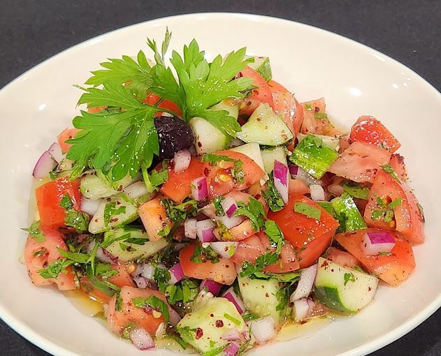 A white plate topped with a salad of tomatoes , cucumbers , onions and olives.