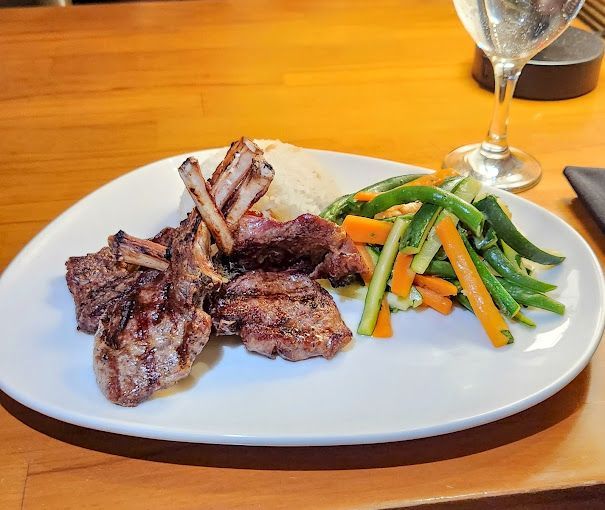 A white plate topped with meat and vegetables next to a glass of wine