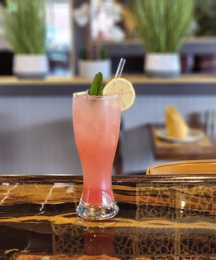 A pink drink with a cucumber and lemon slice on a bar.