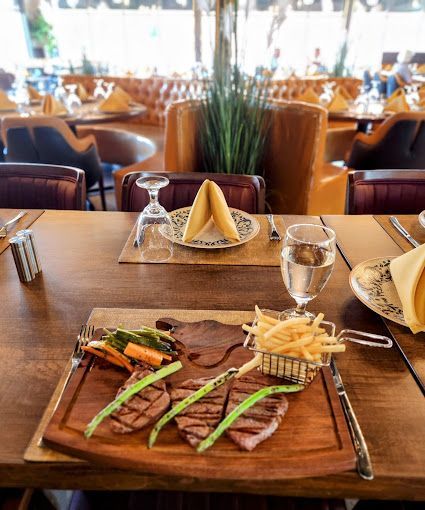 A steak and vegetables on a wooden cutting board on a table in a restaurant.