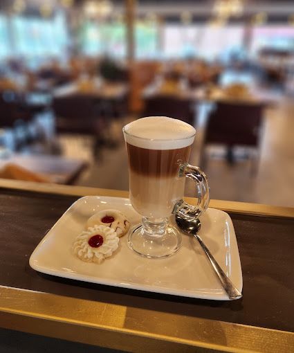 A cup of coffee is sitting on a tray with cookies and a spoon.