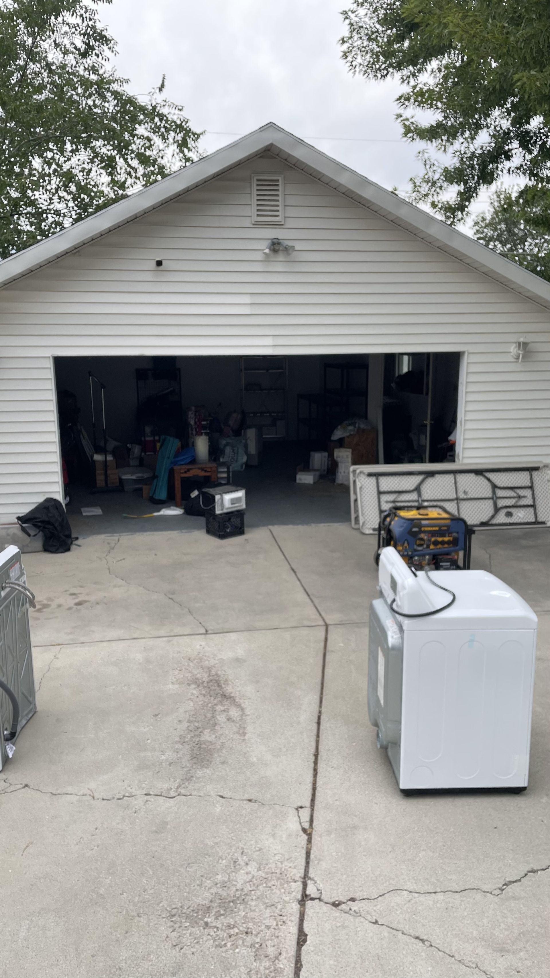 Garage with open door, various items inside and on driveway. A person stands in the garage doorway.