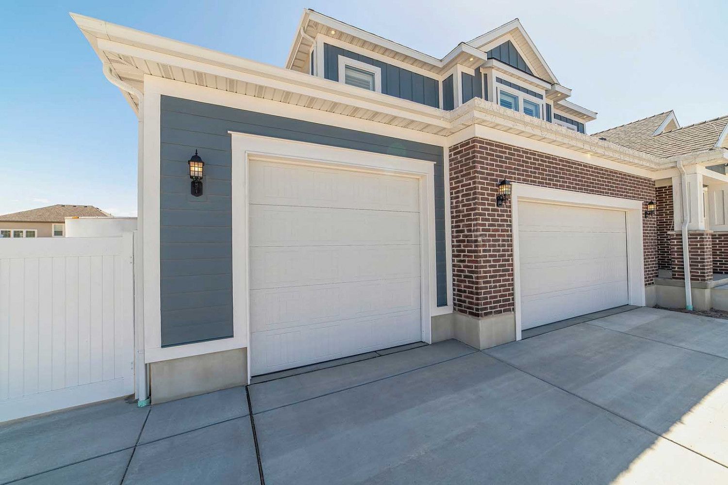 Two-car garage with white doors, blue siding, brick accents, and a concrete driveway.
