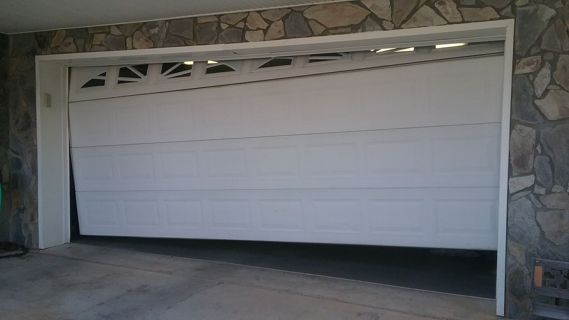 White garage door partially open, against a stone facade.