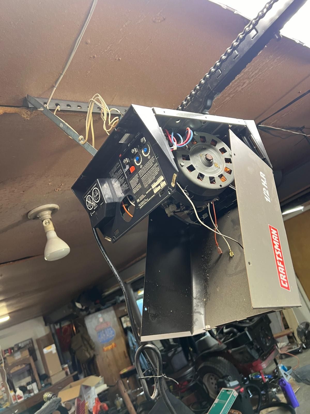Garage door opener, black metal housing, exposed wiring, mounted on ceiling.