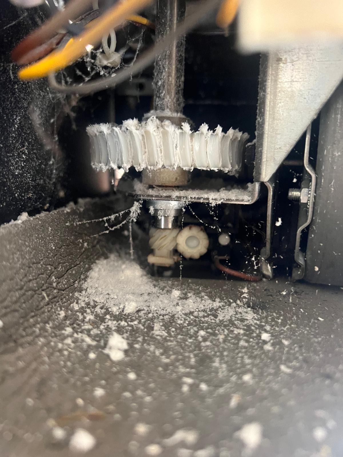 Close-up of a damaged white plastic gear covered in white debris within a machine's metal housing.