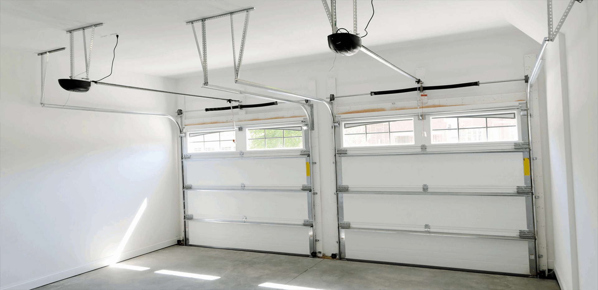 Garage interior with two overhead garage doors, white walls and ceiling, and gray concrete floor.