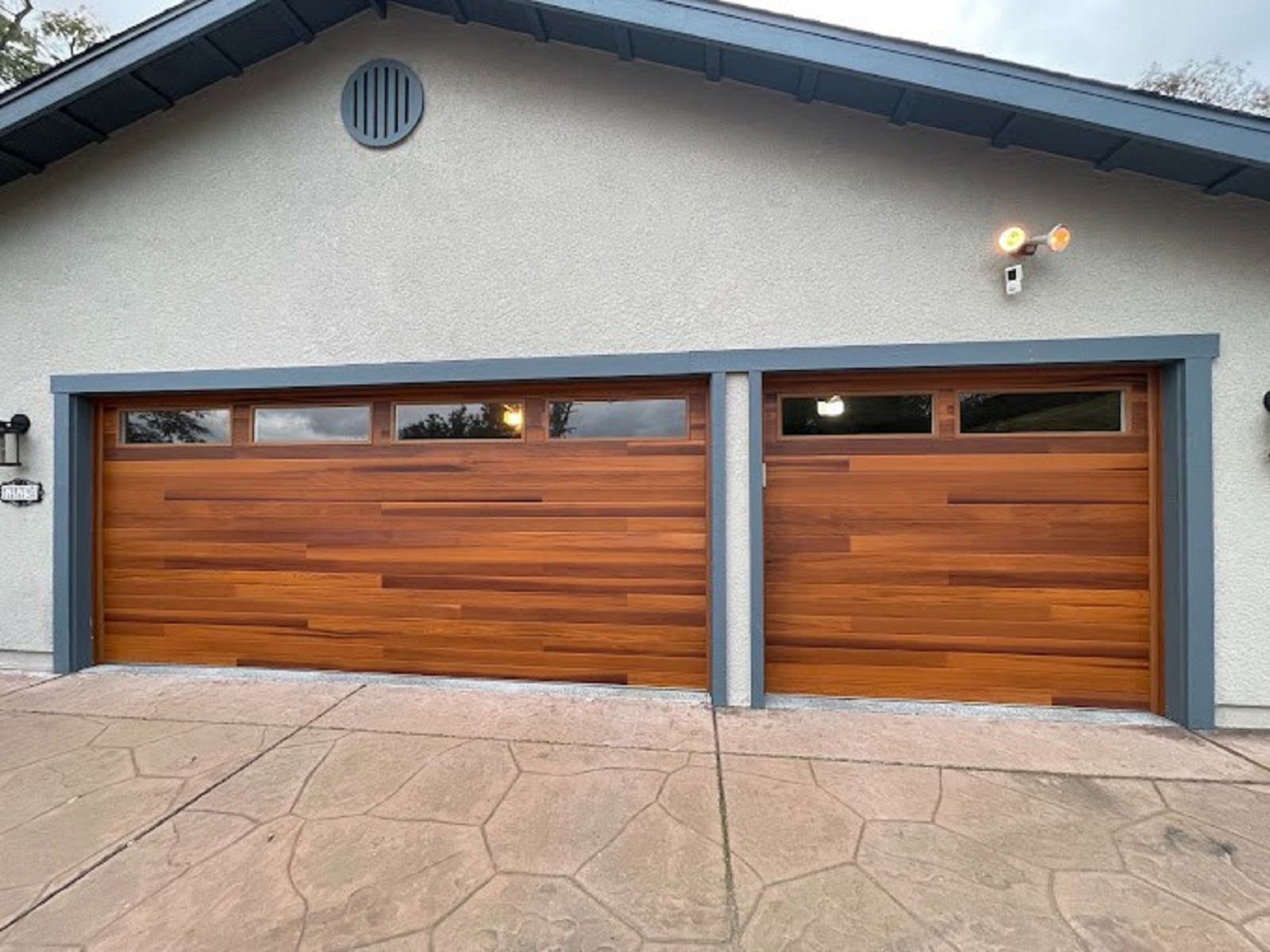Two wooden garage doors with windows, gray trim, and tan siding.