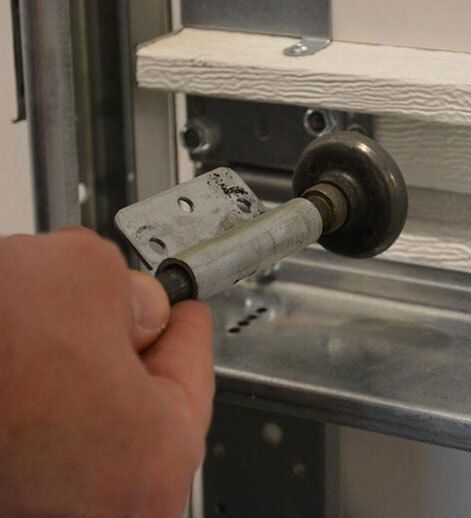 Hand holding a garage door roller and its bracket; roller is removed from track.