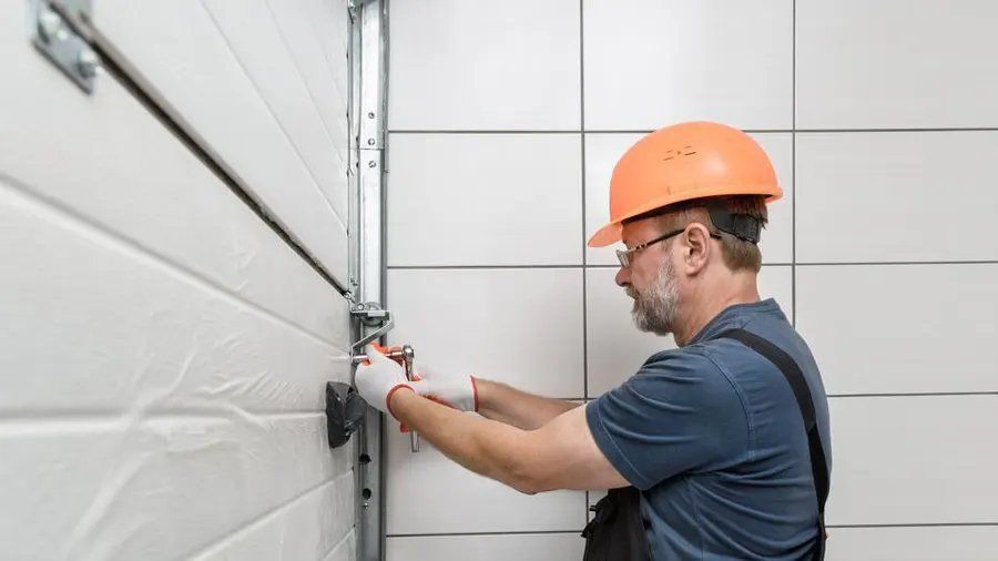 Man in hard hat and gloves repairs garage door mechanism.