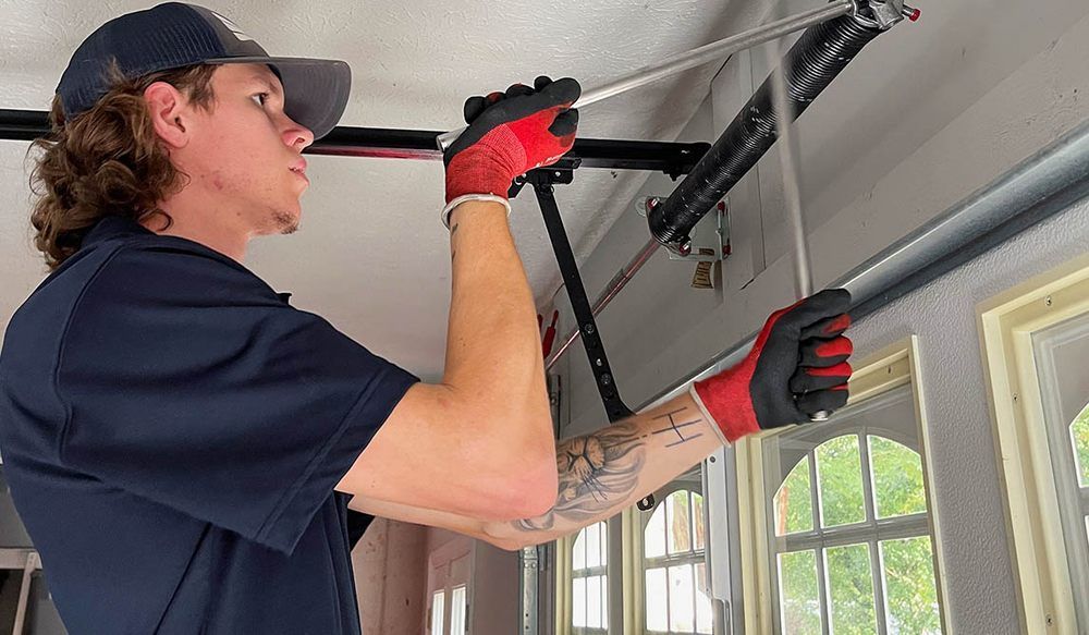 Man in red gloves working on a garage door mechanism, holding a metal bar.