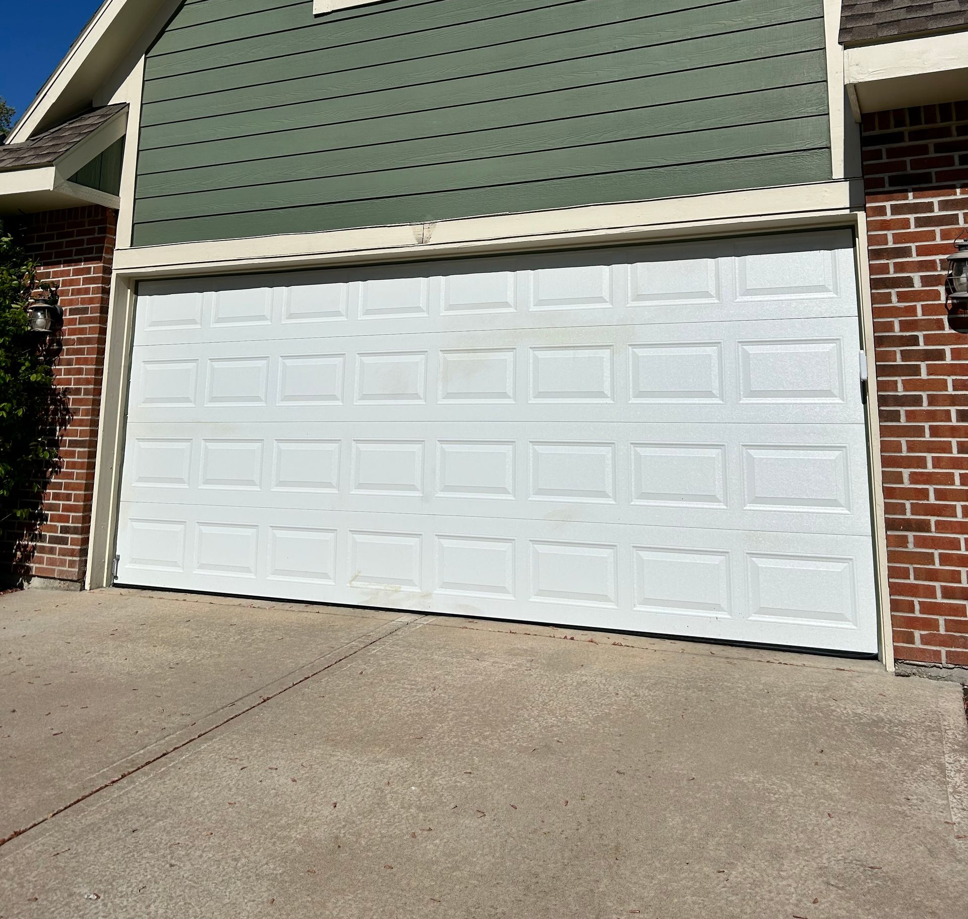 White garage door on a house with green siding and a brick facade, on a concrete driveway.