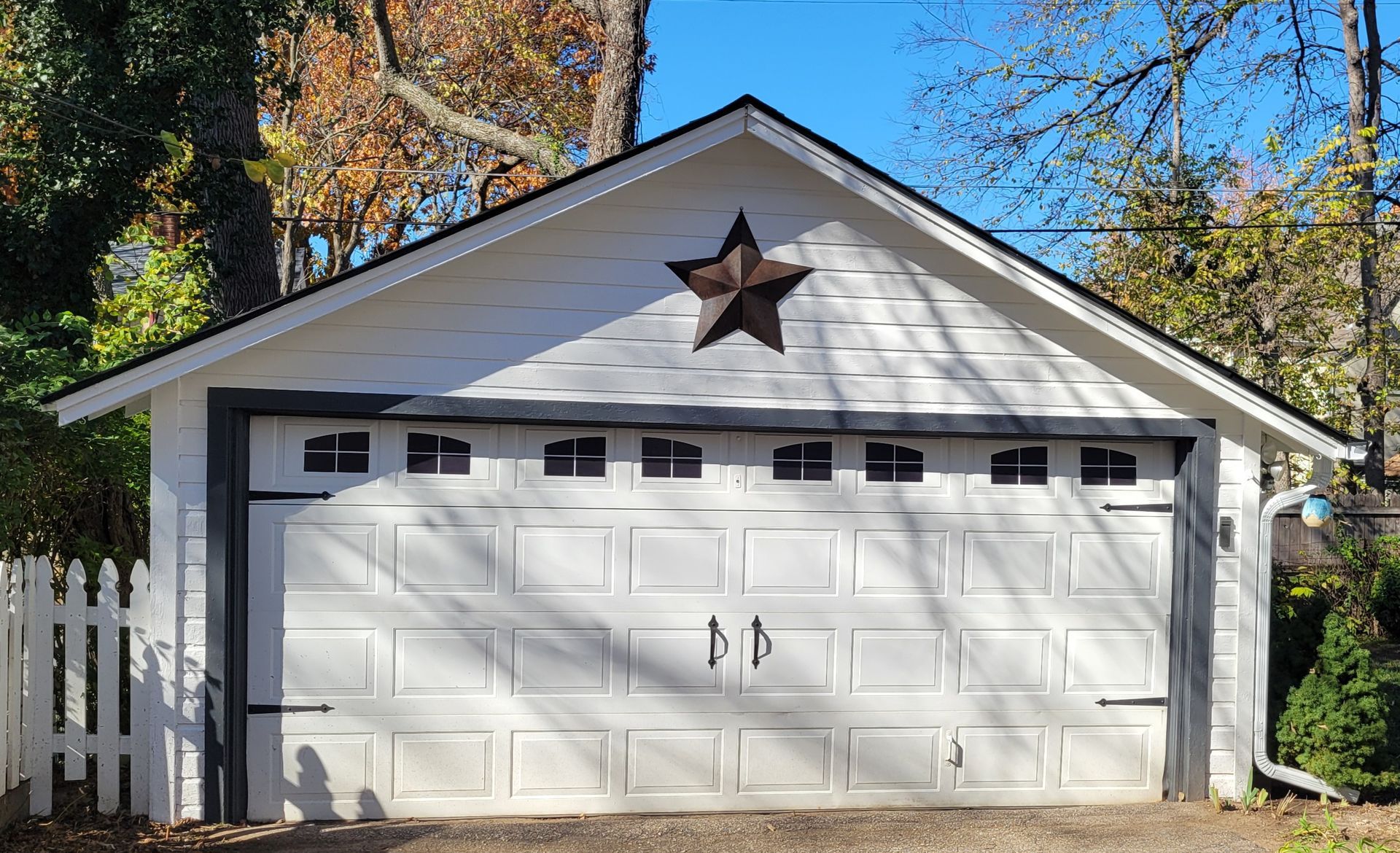 White garage with black trim, star, and white picket fence in front.