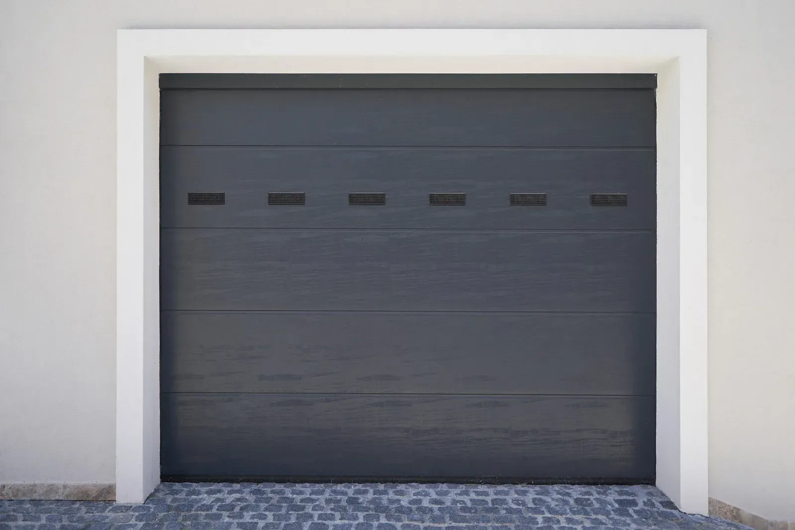 Dark gray garage door with six small horizontal slots, framed by white trim.
