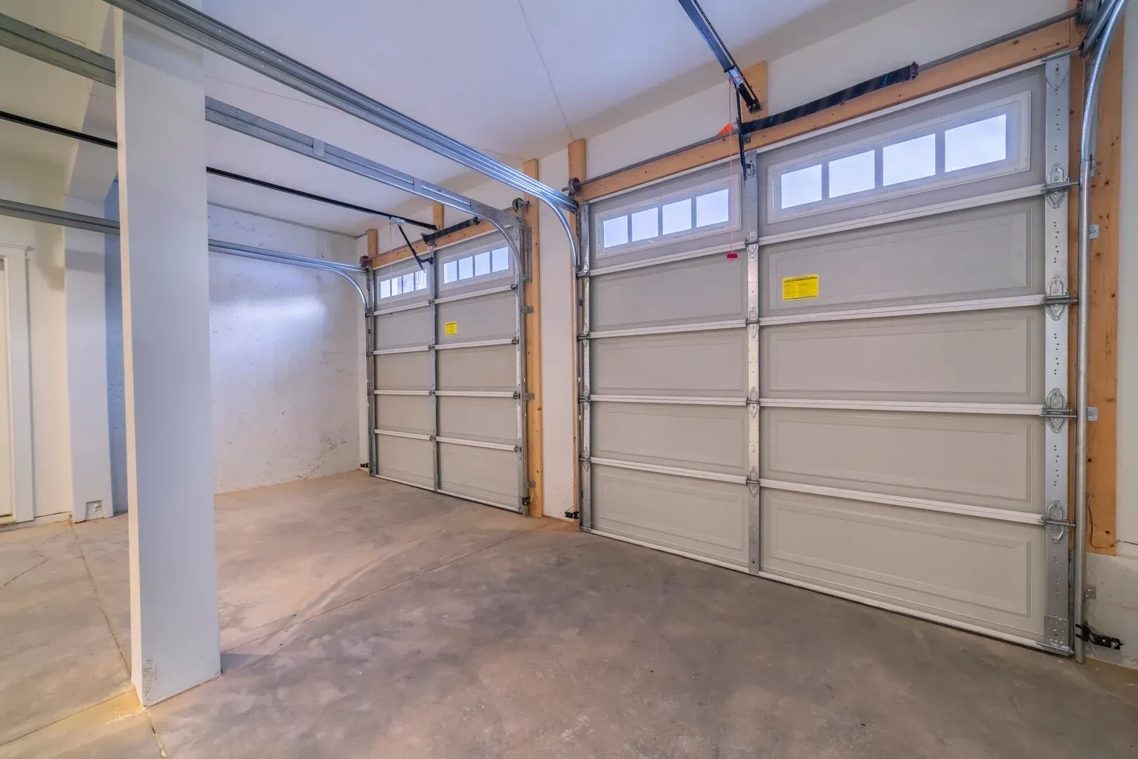 Empty garage interior with two closed white garage doors and concrete floor.