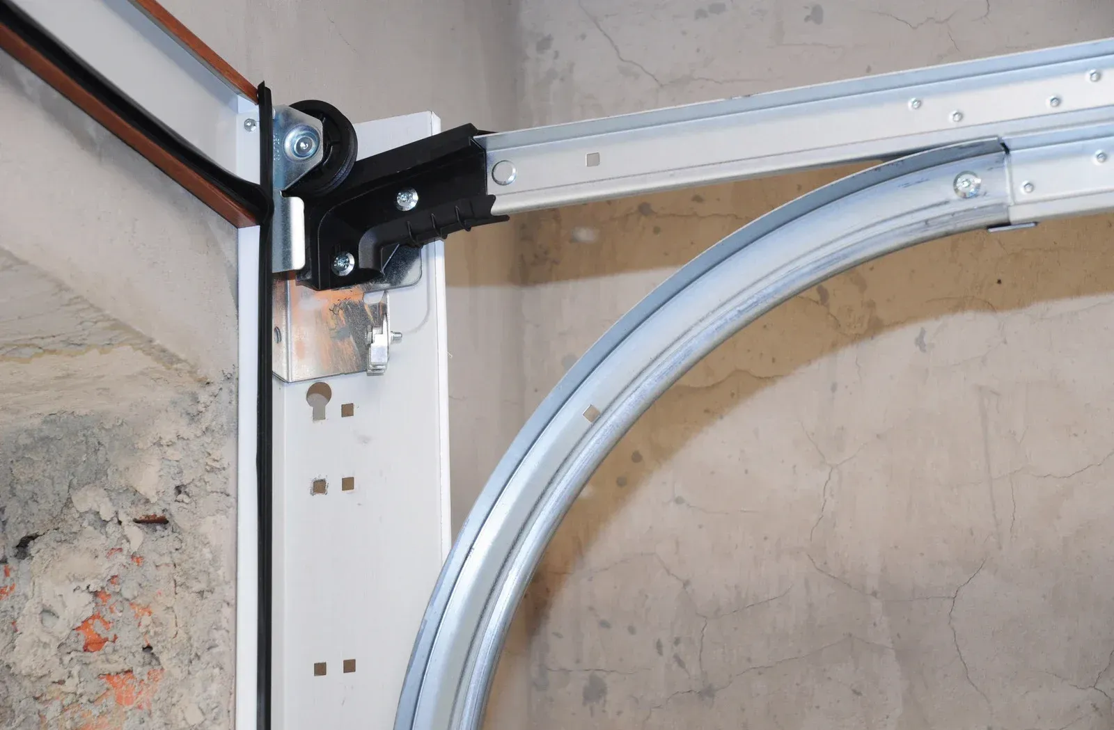 Garage door track and roller assembly: Metal track curves, roller in black bracket, connected to door panel.