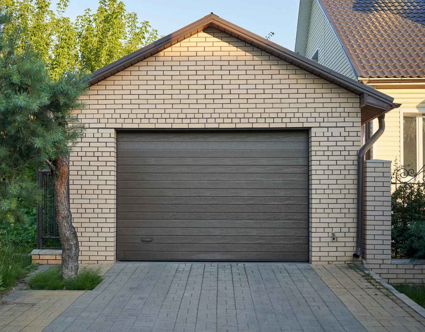 Garage with a brown door and beige brick facade; a driveway leads up to it.