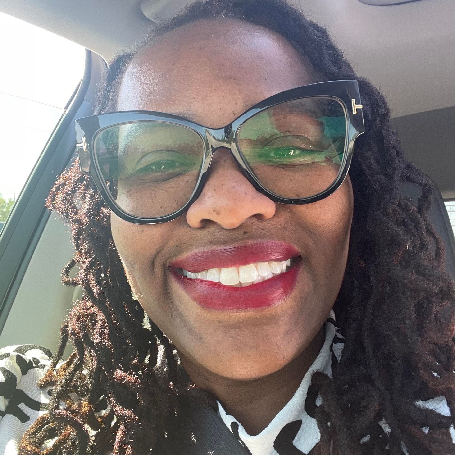 A woman wearing glasses and red lipstick is smiling in a car
