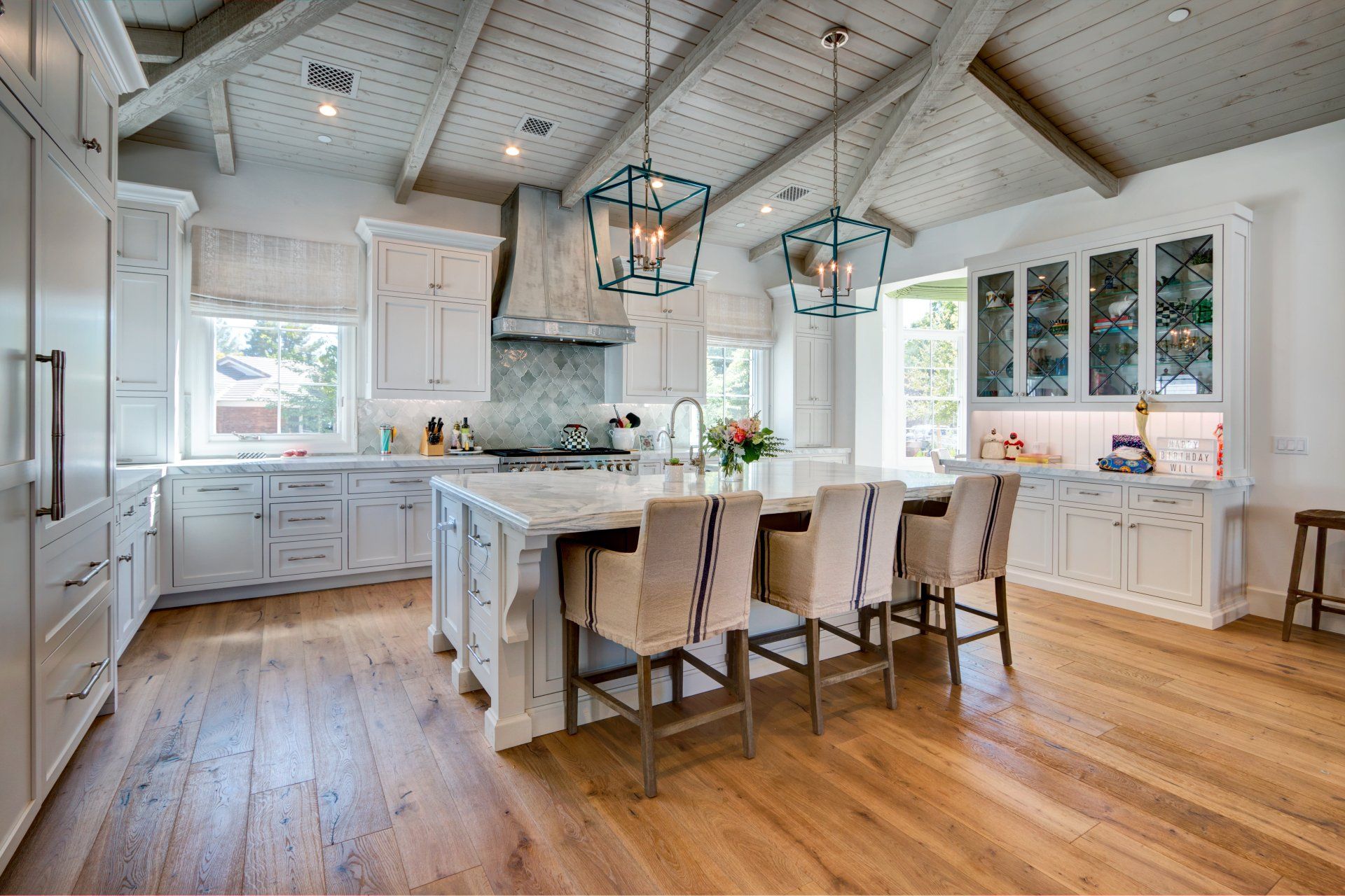 Spacious white kitchen with light wood floors, a large island, and blue pendant lights.