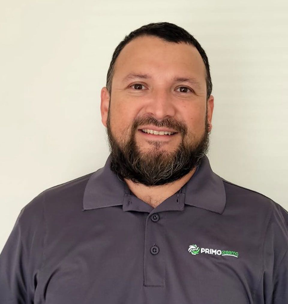 Man with dark hair and beard, wearing a gray polo shirt, smiling at the camera.