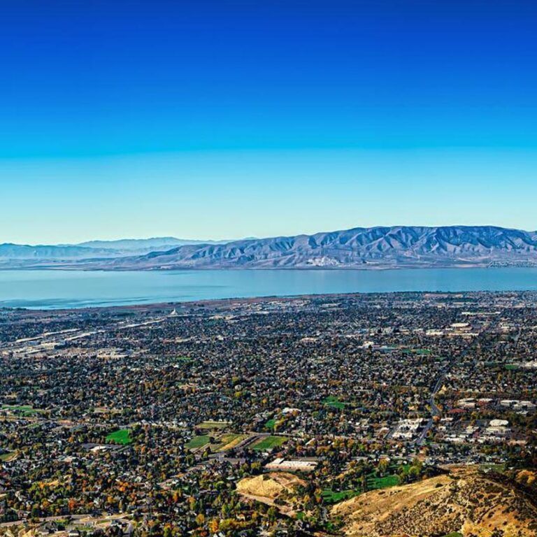 Cityscape with blue lake and mountains under a clear blue sky.