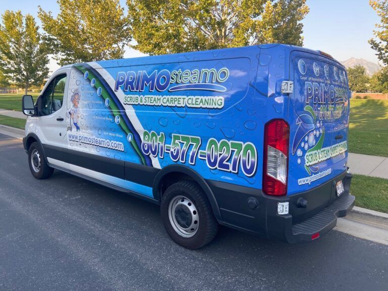 White Primo Steam van with blue graphics and phone number parked on asphalt.