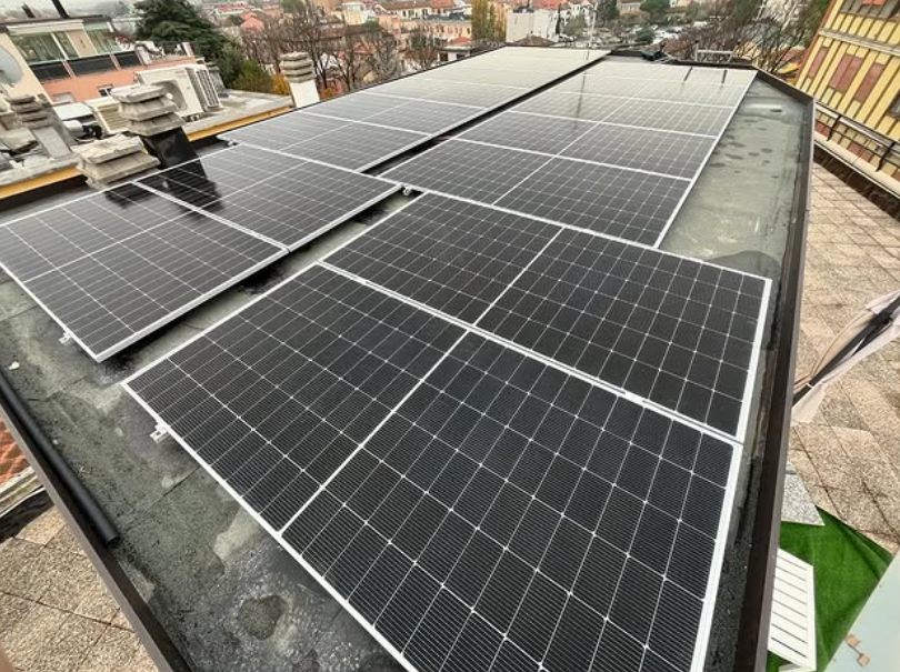 Vista dall'alto di pannelli solari installati su un tetto piano in città, accanto a unità di climatizzazione e camini.