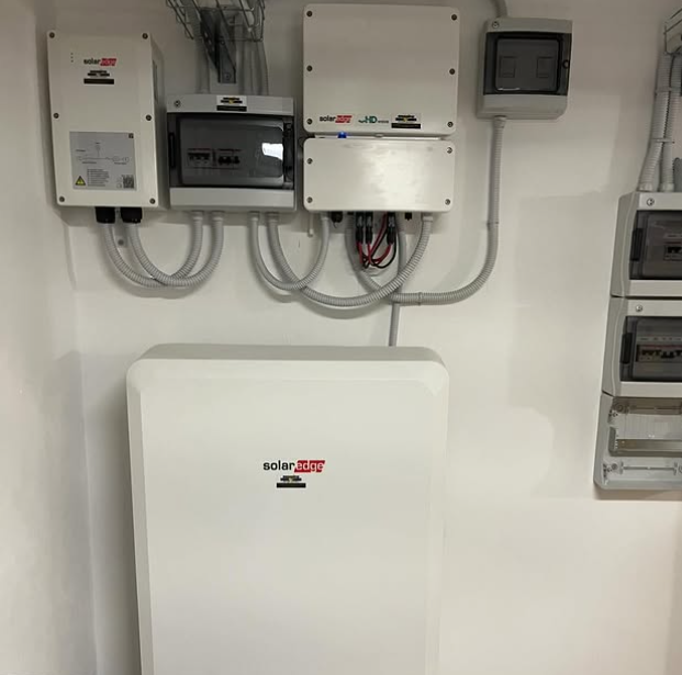 Apparecchiature per l'energia solare di colore bianco, tra cui batterie e pannelli elettrici, montate su una parete bianca e pulita.