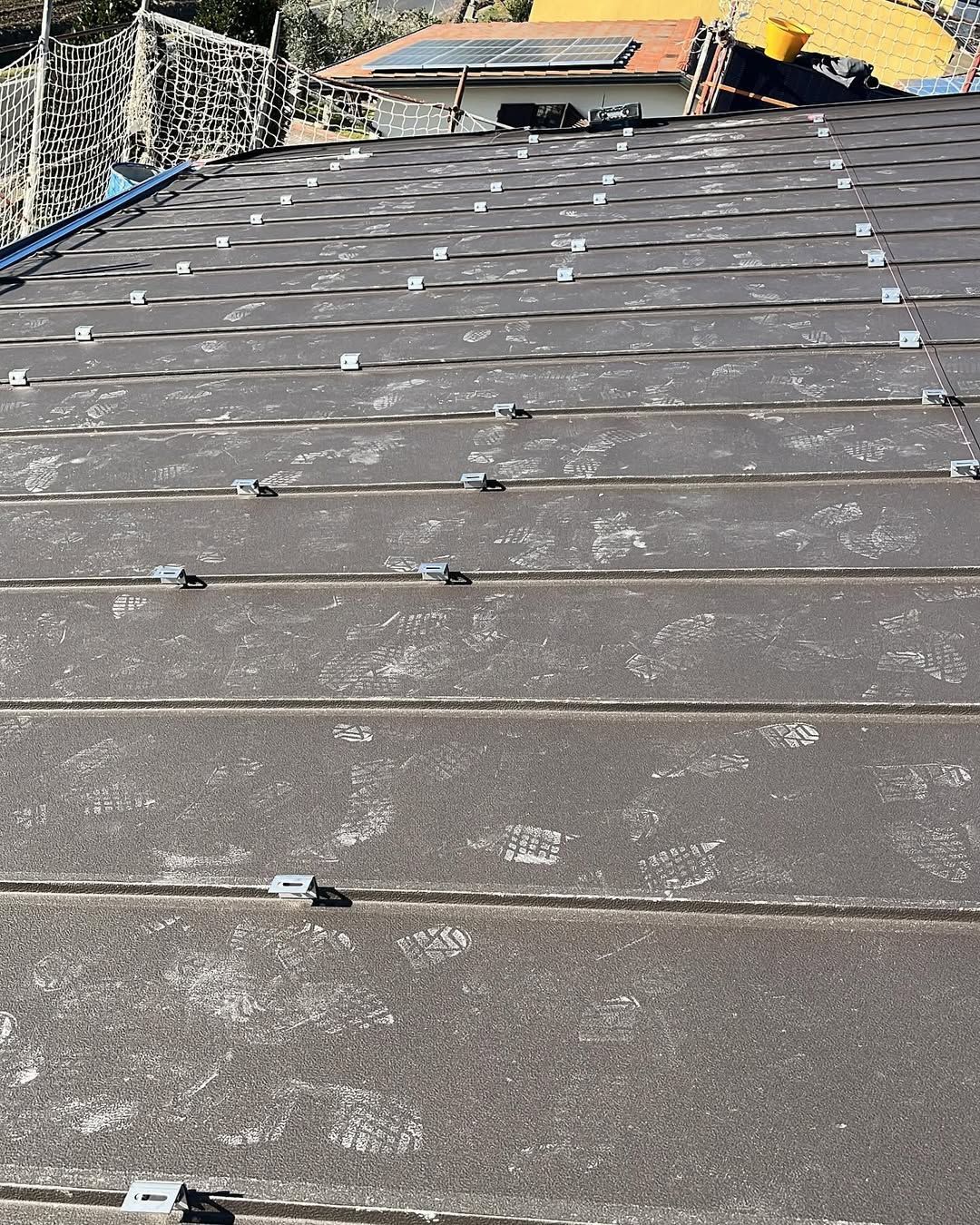 Un tetto in metallo grigio ricoperto da motivi a impronte bianche, con clip di fissaggio installate in file per i pannelli solari.