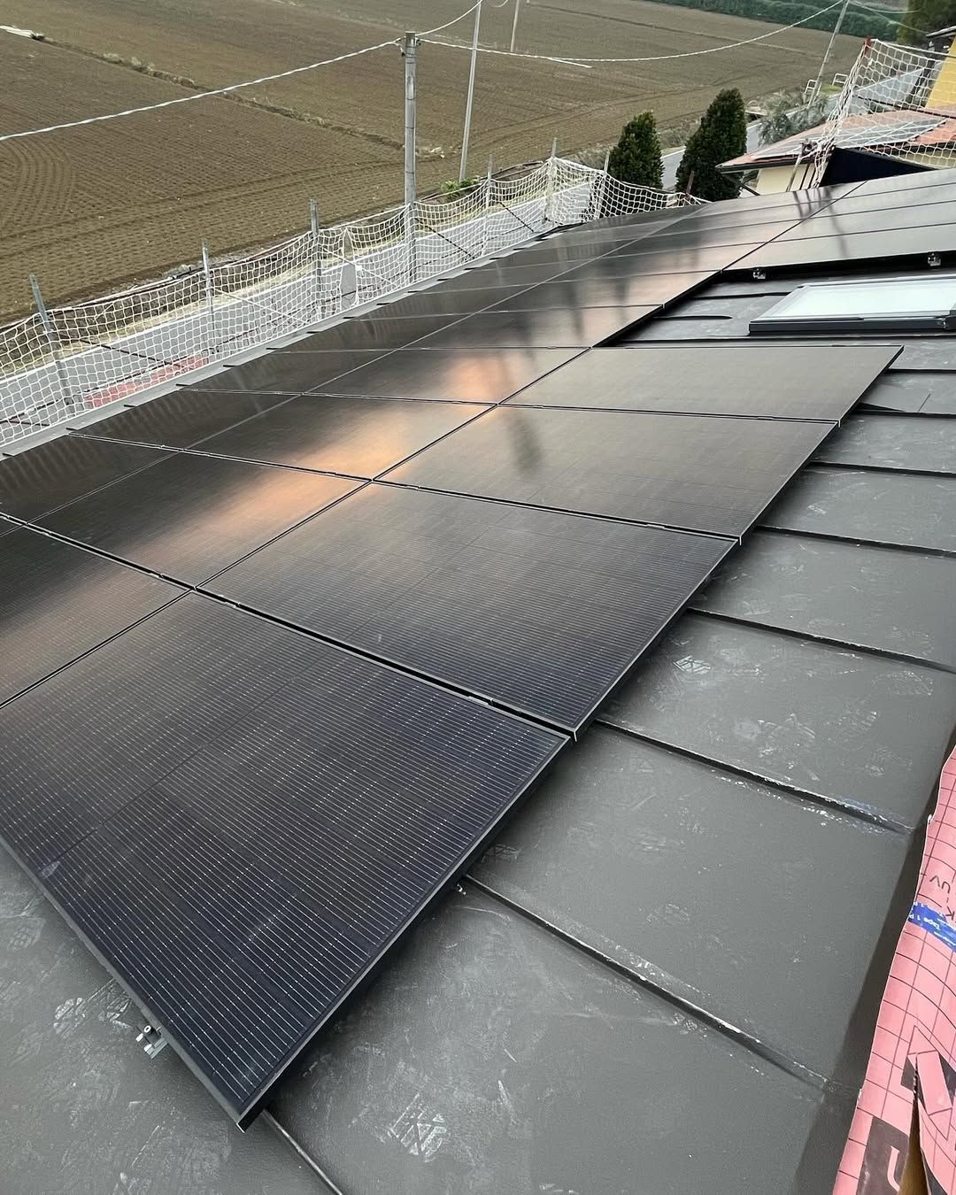 Pannelli solari neri installati su un tetto di metallo scuro, con un campo visibile sullo sfondo.