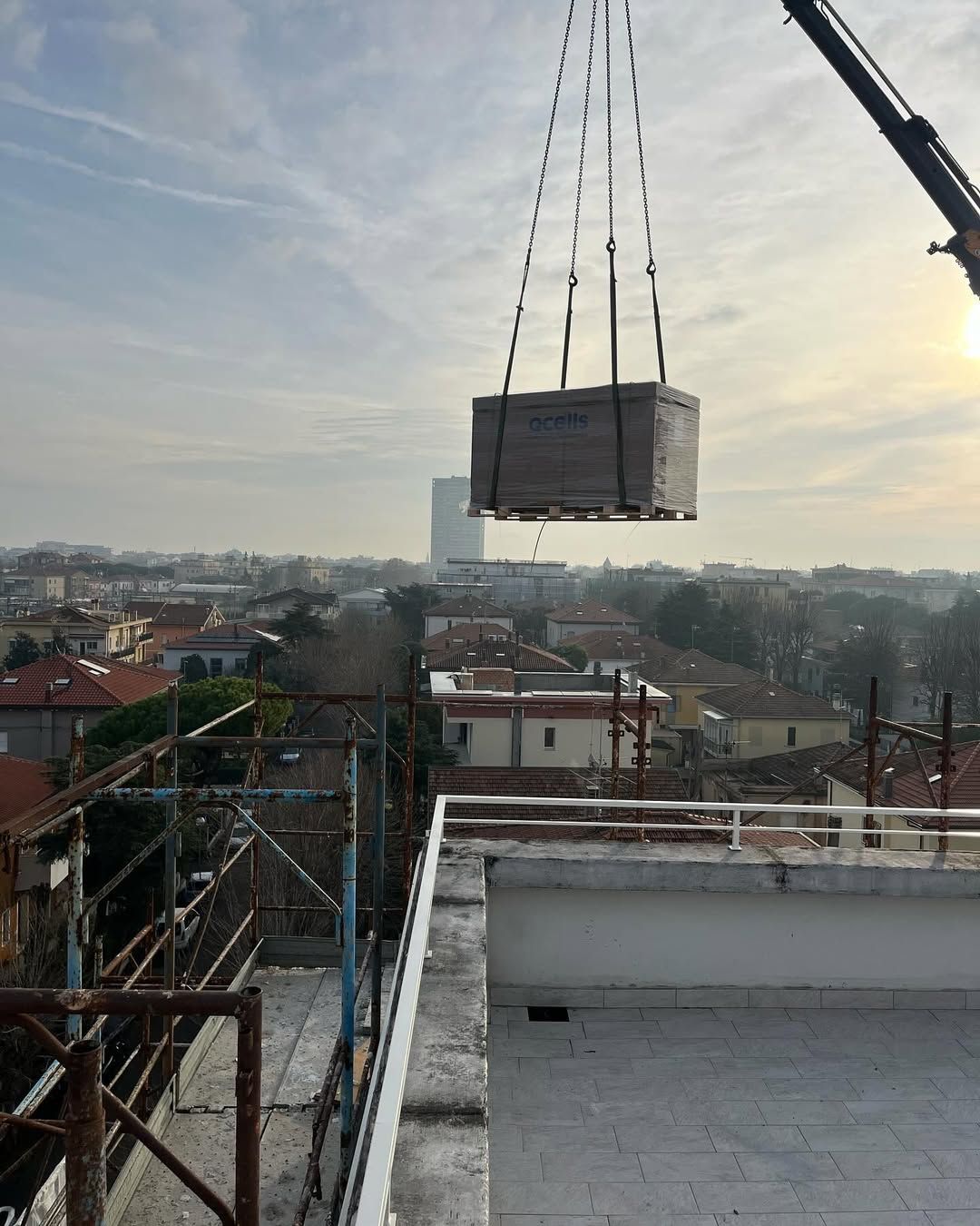 Al tramonto, una gru da cantiere solleva un grande pallet quadrato di materiali edili sopra lo skyline della città.