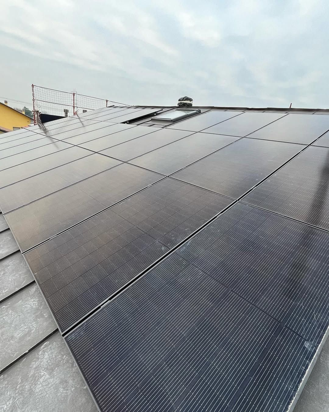 Vista di un tetto ricoperto di pannelli solari neri, con un piccolo lucernario visibile vicino alla sommità.