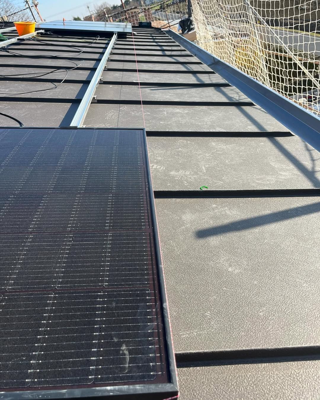 Pannelli solari in fase di installazione su un tetto piano e scuro con struttura metallica, in prossimità di una rete di sicurezza.