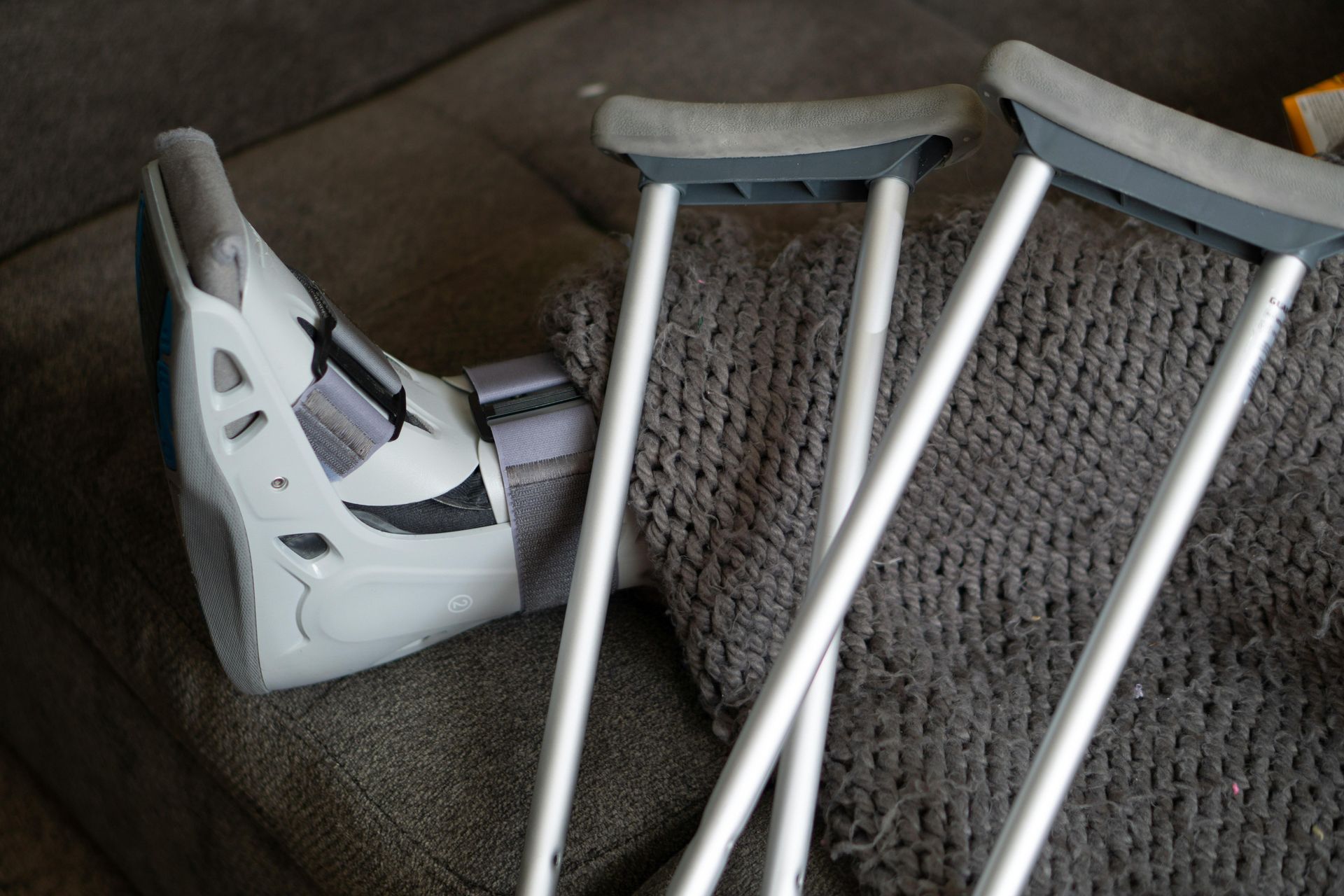 A person with a cast on their foot is laying on a couch next to crutches.