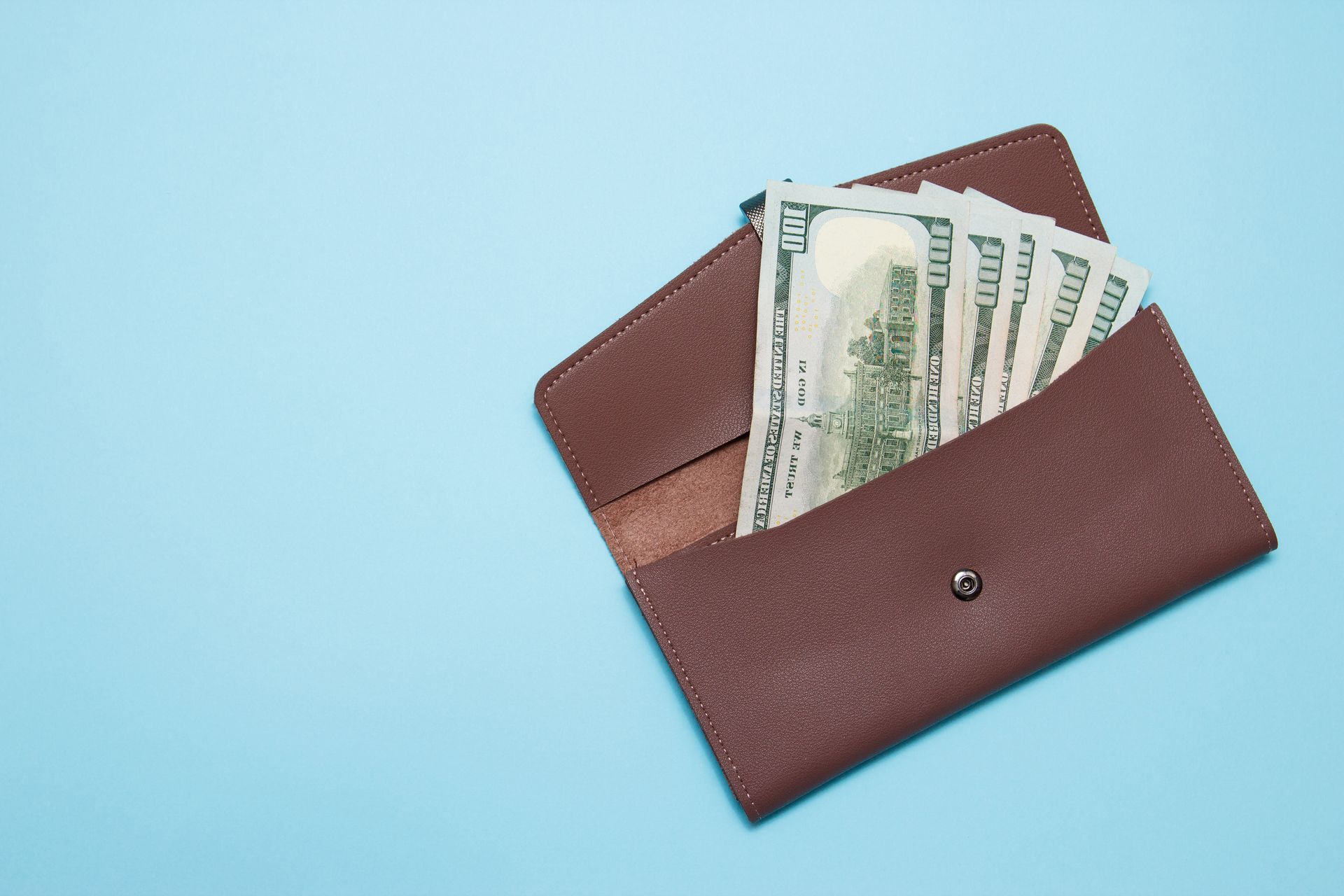 A brown wallet filled with money on a blue background.