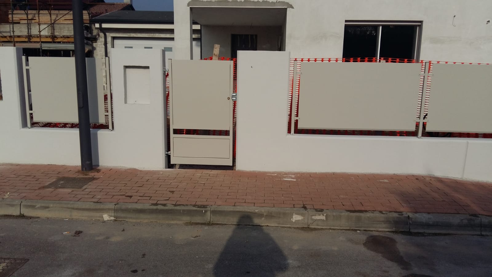 Edificio bianco con marciapiede in mattoni, cancello in metallo e recinzione in metallo rosso.