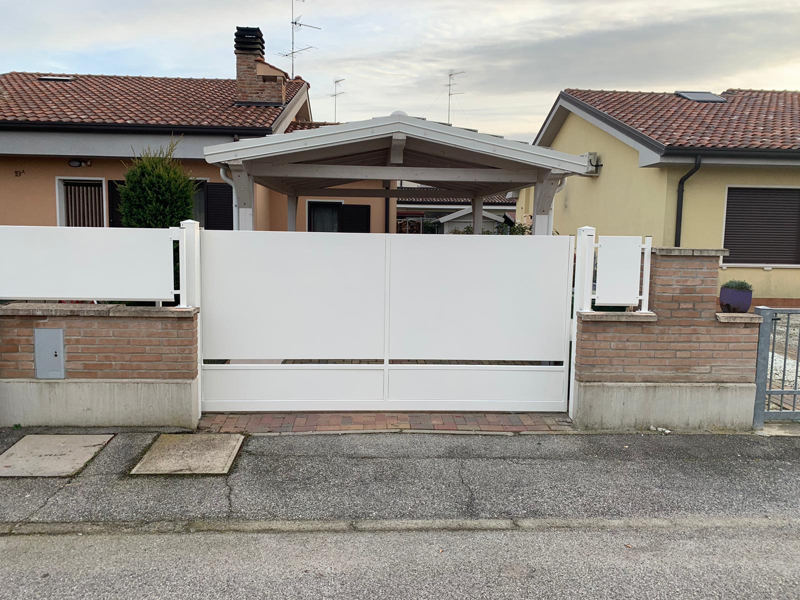 Cancello bianco con pareti intonate, ingresso di una casa. Sullo sfondo, case con tetti di tegole rosse.