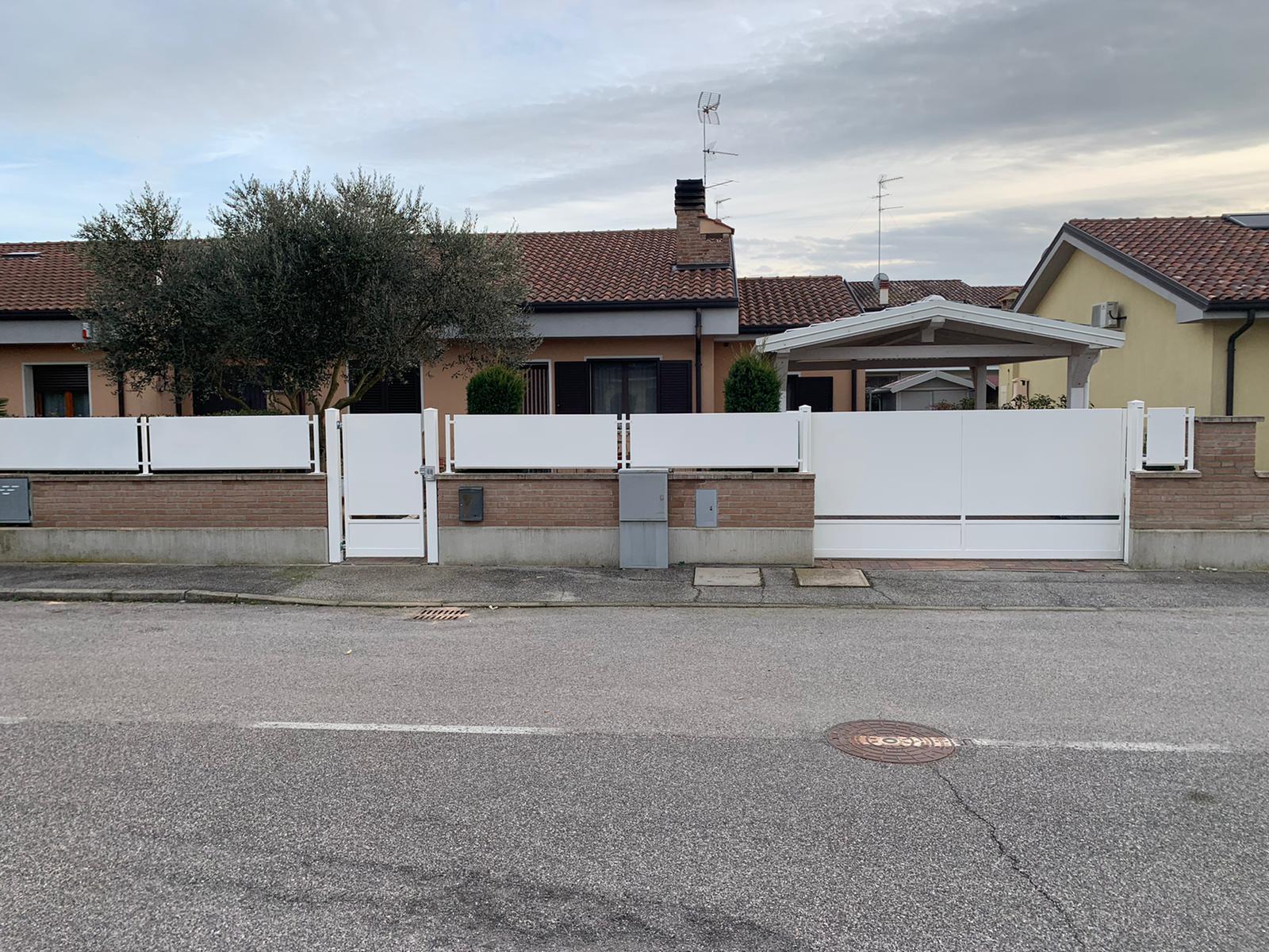 Recinzione bianca e cancello davanti a una casa in mattoni e stucco, con un cielo nuvoloso sopra di noi.