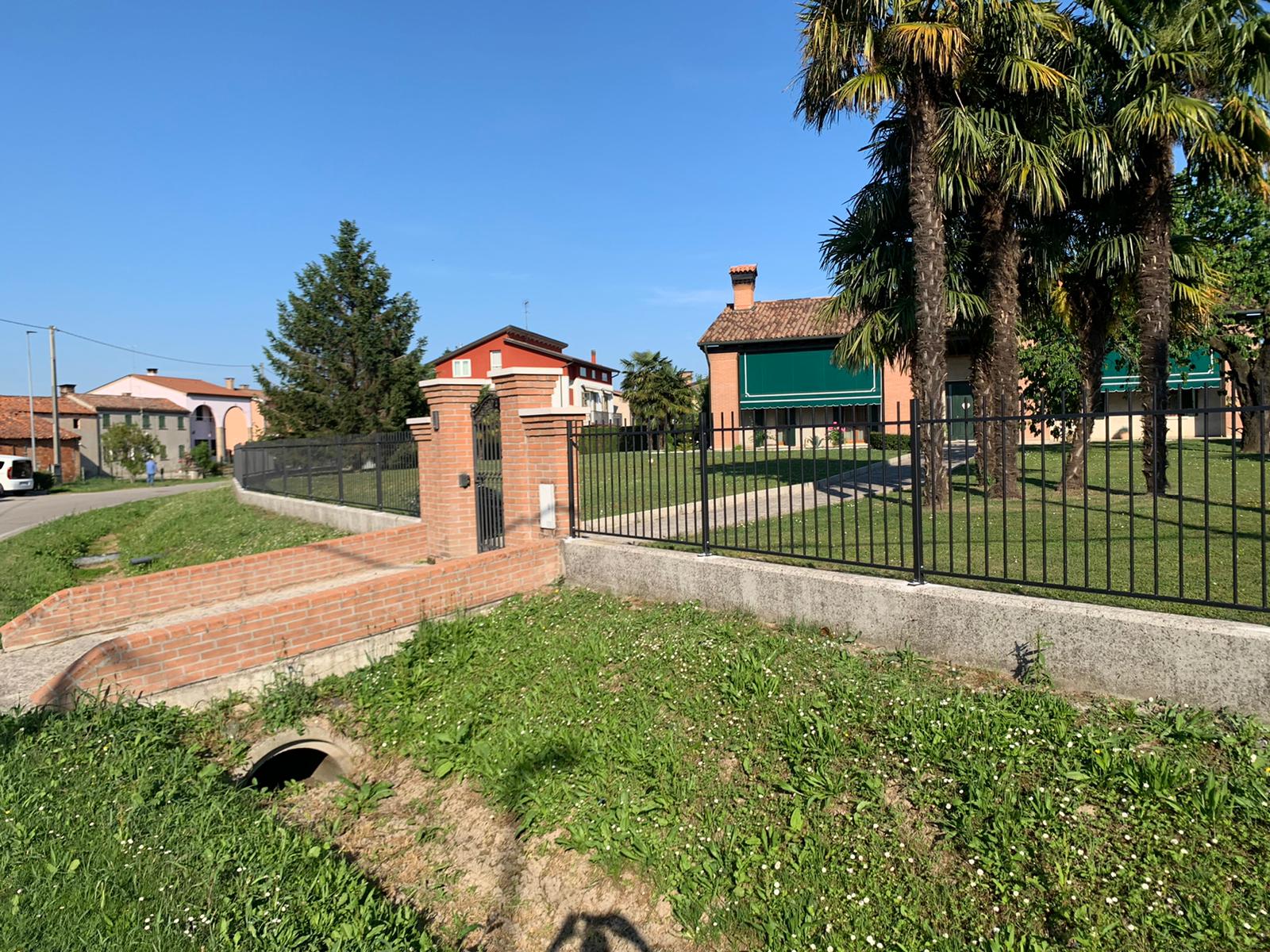 Argine erboso con muratura e recinzione. Case e palme sullo sfondo in una giornata di sole.